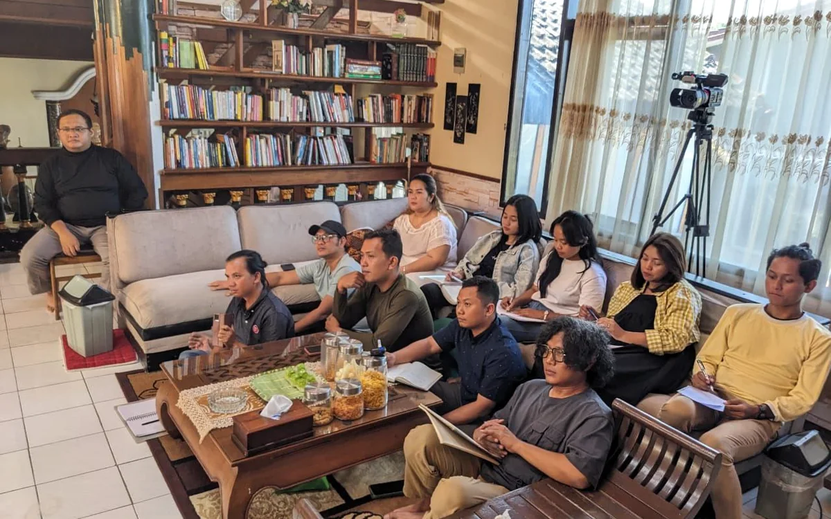 Peserta duduk dengan catatan di ruang yang memiliki rak buku.