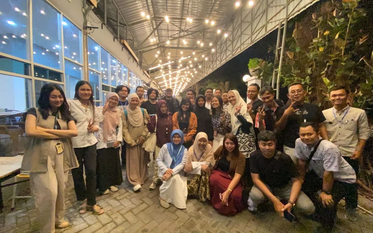 Sekelompok anggota komunitas berfoto bersama di ruang terbuka dengan lampu hangat.
